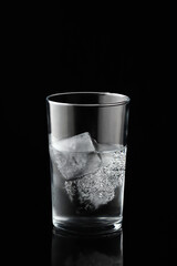 Cold water and ice cubes in glass on black background