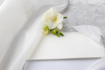 Wedding blank and an envelope with a delicate freesia flower on a light table.