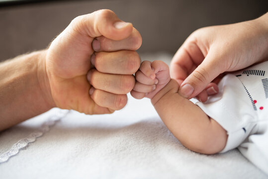 Fist of newborn baby and father with support of mother's hand, family photo, selective focus