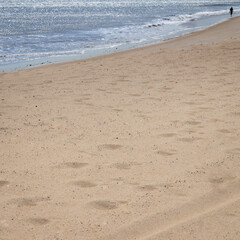 Small human silhouette walking on a deserted beach.