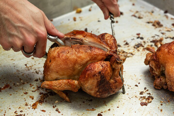 the hands of an unrecognizable cook slicing the roasted chicken