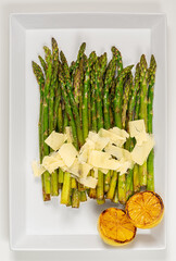 Grilled green asparagus with lemon and parmesan on big white plate. Healthy food concept. Top view.