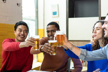 Multiethnic friends drinking beer at brewery bar restaurant on weekend - Friendship concept with young people having fun together toasting brew pint on happy hour at pub - Focus on middle Eastern man