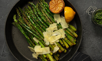 Fried green asparagus with lemon and parmesan in a pan.  Black marble table with olive oil and...