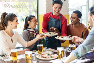 Fototapeta na wymiar Confidant waiter serving delicious pizzas margherita to multicultural friends in cozy pizzeria restaurant - Multiethnic friends having fun together at the pizzeria eating pizza and drinking blond beer