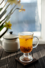 sea buckthorn warm drink. Morse on the windowsill against the background of flowers Daffodils in early spring.