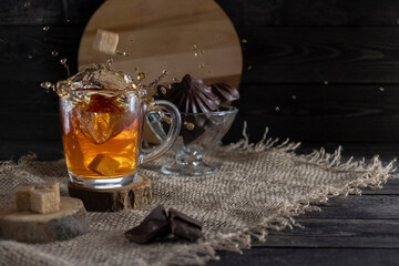 splash tea and marshmallows in chocolate and cane sugar on burlap on a dark rustic wooden background