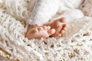 Tiny foot of newborn baby. Soft newborn baby feet against a beige  blanket. Baby feet with toes curled up