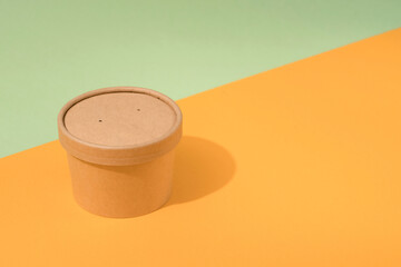 Disposable kraft paper street food container or cup with paper cap on orange and green background with copy space, mockup. Sustainable food packaging concept