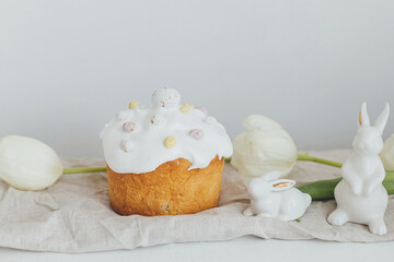 Happy Easter! Homemade easter bread, bunny, white tulips on rustic table in room. Modern easter table setting. Stylish freshly baked easter cake with sugar glaze and sprinkles.