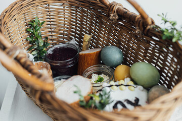 Traditional Easter basket. Natural dyed easter eggs, easter bread, ham, beets, butter, cheese in wicker basket decorated with green buxus on rustic wooden table. Top view