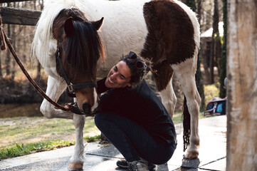 Caucasian female, horse owner, smiling and washing white pony's leg while talking to it