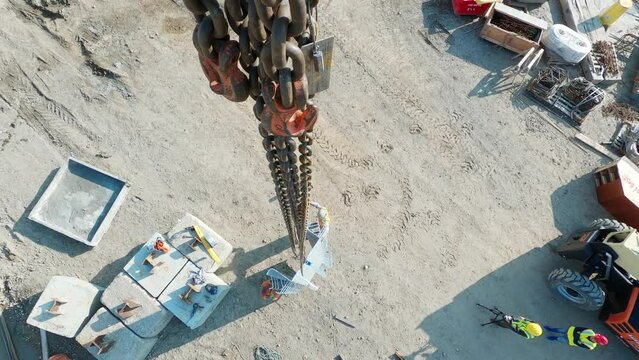 POV top down, construction tower crane chains moving equipment, supporting workers on site