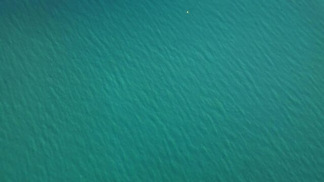 Aerial drone footage of turquoise clear water beach in early morning light, filmed with a slow tilt up