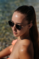 A beautiful young woman in glasses and a bikini is sitting on the ocean and enjoying a vacation on a sunny day. Tourism and tourist trips. Opening borders, and vacation.