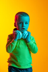 Portrait of cute little boy with huge headphones isolated on yellow studio backgroud in neon light. Concept of child emotions, facial expression, childhood