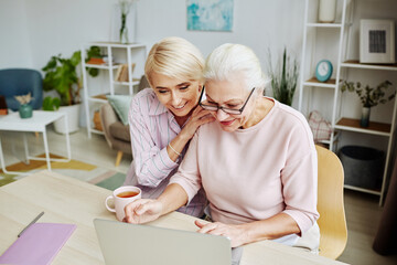 Portrait of smiling young woman helping senior mother using computer in cozy home interior
