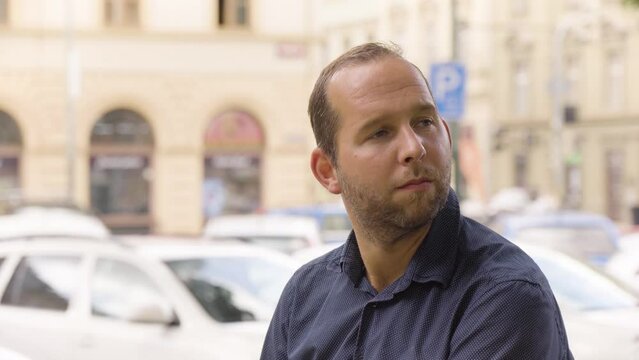 A Caucasian man thinks about something with a smile in an urban area - closeup - a colorful street in the blurry background