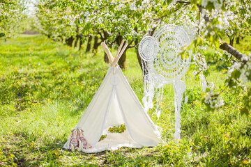 Photo zone for a children's photo shoot in a spring blooming garden - wigwam, crocheted dream catchers and rabbit toys © Kathleen