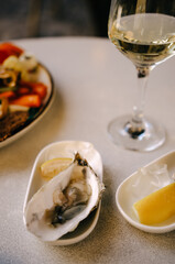 Oysters in white plate with lemon and glass of wine on white table