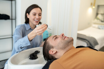Obraz na płótnie Canvas Beautician applying hair serum on mans head