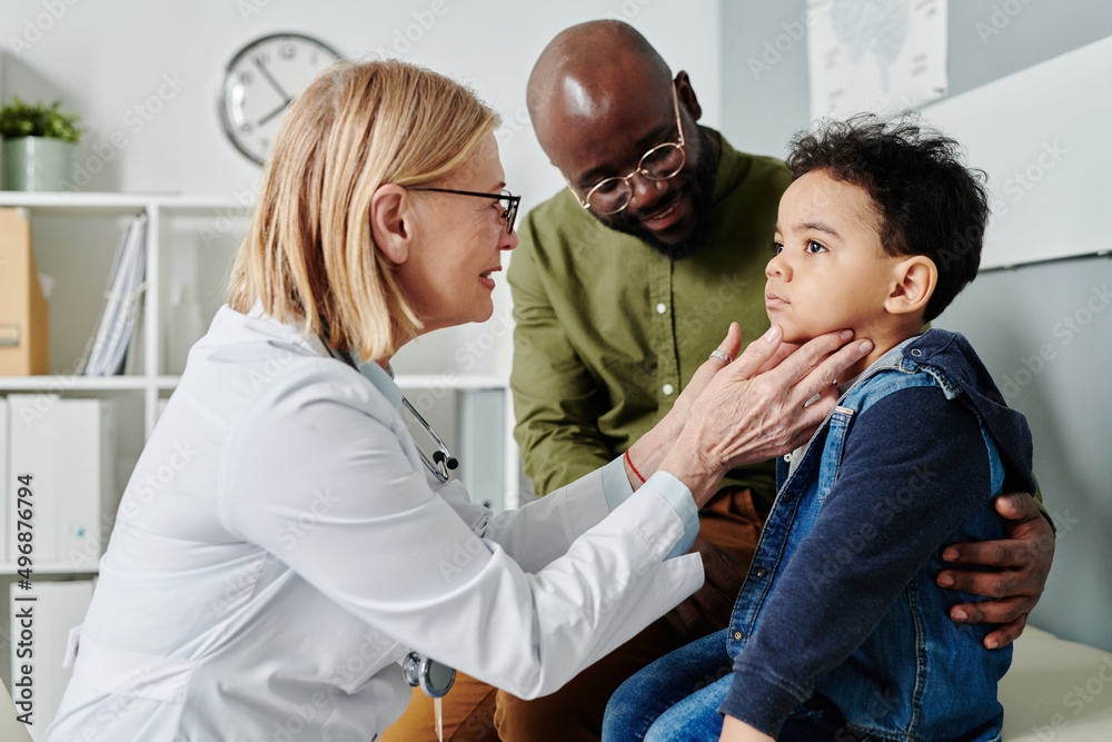 Poster experienced emale endocrinologist touching neck of little child while checking his thyroid during vi