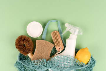 Organic household cleaners made of natural ingredients, bamboo brush, organic dishcloth, lemon, baking soda, citric acid in cotton net bag on green background. Mockup. Green cleaning concept