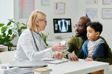 Confident experienced doctor prescribing new medicament to young man with his little son sitting by...