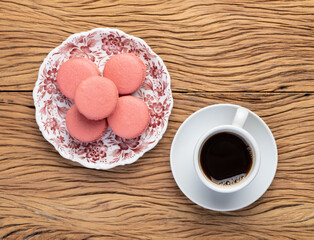 Berry macarons on a plate with coffee over wooden table