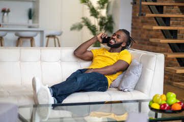 Fototapeta premium Man reclining on sofa talking on smartphone