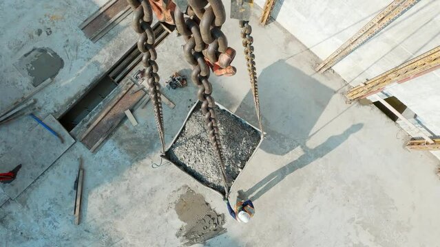 POV top down, container full of gravel lifted up by tower crane chains at construction site