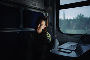 Fototapeta na wymiar Portrait of a young woman riding in a train with a laptop on the table and looking at the camera with a serious face.