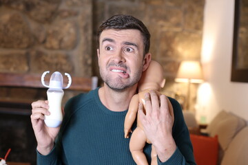 Frustrated man holding baby doll and feeding bottle