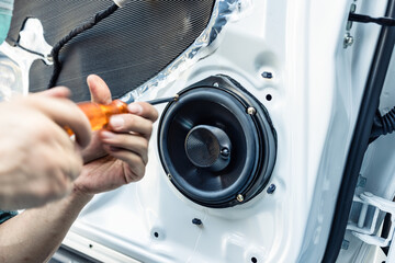 Mechanic using screwdriver screwing drywall screw with car speaker on vehicle door
