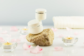 Fototapeta na wymiar Mock up beauty products. White cosmetic jars on a stone podium, blurry rose petals and candles on a white table with copy space. Soft image and soft focus style. Flower organic cosmetic product
