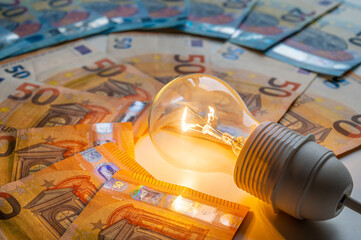 Fototapeta Light bulb turned on, with Euro banknotes around. Increase in electricity tariffs, energy dependence, energy sources and energy supplies.
 obraz