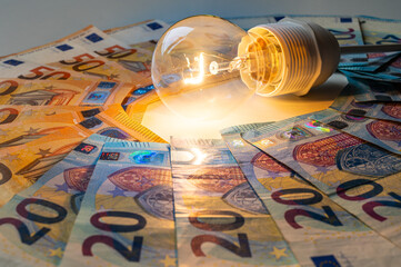 Light bulb turned on, with Euro banknotes around. Increase in electricity tariffs, energy dependence, energy sources and energy supplies.
