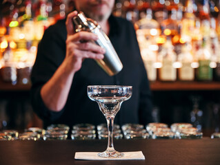 Male bartender making a cocktail with a shaker behind the bar counter at the pub