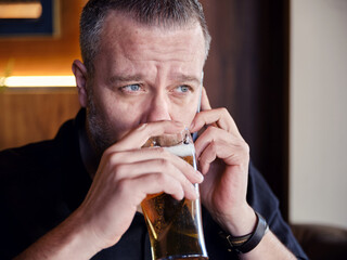 Close up portrait of a hipster man drinking a glass of beer and talking on the mobile phone in a bar or pub.