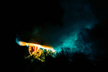 A man in a gas mask with an umbrella and colored smoke, photo at night