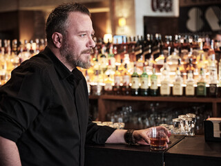 Portrait of a handsome mature man holding a glass of neat whiskey at the bar or pub.