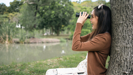 Cute Asian woman is taking a nature tour by the river.Woman with black hair is enjoying using binoculars to observe nature such as animals,birds,trees, and the abundance of forests.excited expression.