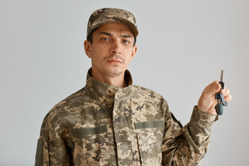 Indoor shot of serious Caucasian man soldier wearing camouflage uniform and cap, posing in his new...