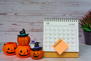 White October 2022 calendar with Jack o lantern pumpkin on wooden desk.