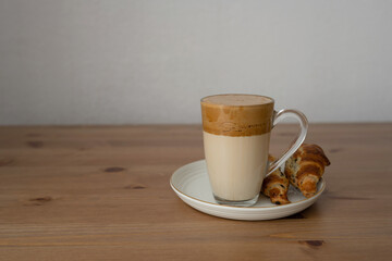 Dalgona coffee in a glass on a wooden table, with croissants.