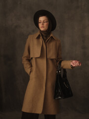 A beautiful young woman poses in the studio on a gray background. Vintage look. Autumn or spring coat, black hat and scarf. Large eye arrows.