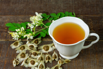 Moringa Tea in white ceramic cup with fresh green leaf and flower on wooden background. Moringa oleifera tropical herb healthy lifestyle concept.
