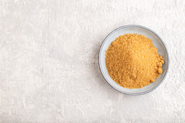 plate with unrefined golden cane sugar on gray concrete. top view, copy space.