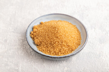 plate with unrefined golden cane sugar on gray concrete. side view, close up.