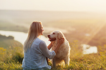 Special and serene moment as a girl is lovingly hugging her Golden Retriever Dog against the sunsetting sky.